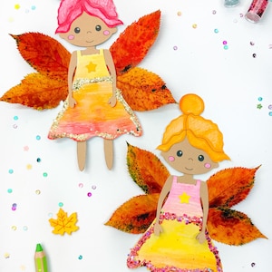 Pode incluir: Duas fadas de papel com folhas de outono para asas. As fadas usam vestidos amarelos e rosa com detalhes de glitter. As fadas estão sobre um fundo branco com confete colorido.