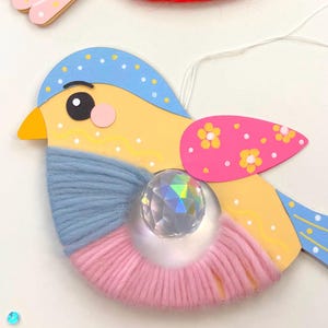K&ouml;nnte beinhalten: Handgefertigte Vogelornamente mit gelben, blauen, rosa und roten Akzenten. Jeder Vogel hat einen Kristallschmuck und Garndetails. Die Fl&uuml;gel sind mit floralen Mustern verziert. Diese skurrilen Dekorationen sind perfekt, um jedem Raum einen Farbtupfer zu verleihen.