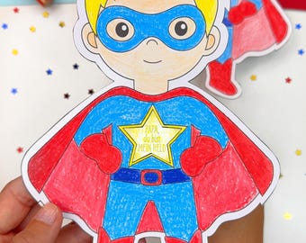 May include: Hand-drawn superhero card with a blue and red costume, yellow hair, and a blue mask. The card has the text "PAPA du bist MEIN HELD" on a yellow star. A second superhero card is visible in the background.