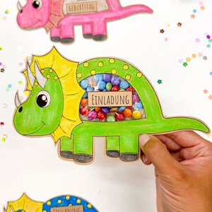 Pu&ograve; includere: Tre inviti a forma di dinosauro con una finestra ritagliata per le caramelle. I dinosauri sono rosa, verdi e blu. Gli inviti dicono "Einladung zum Geburtstag", che si traduce in "Invito al compleanno".