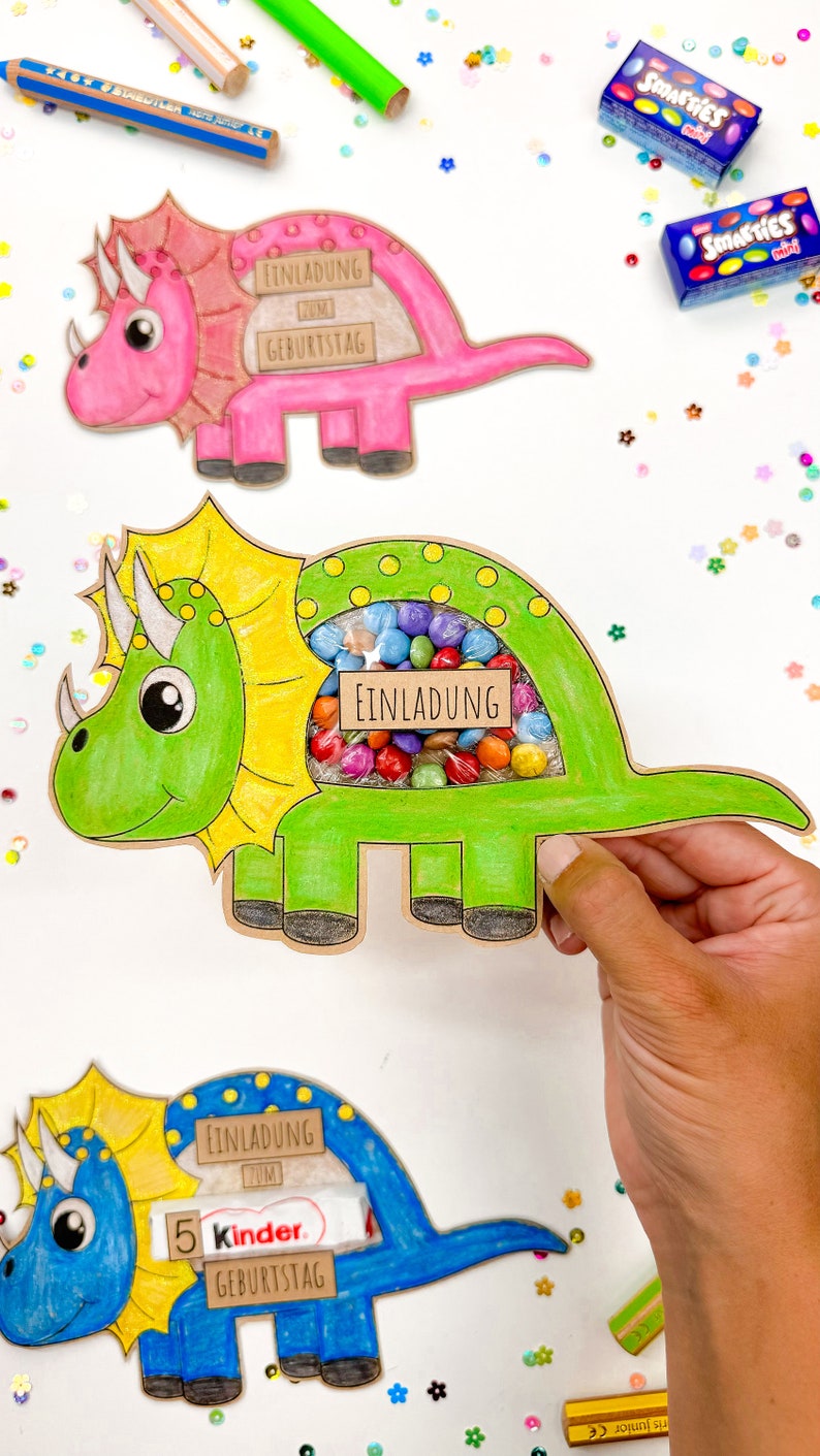 Pu&ograve; includere: Tre inviti a forma di dinosauro con una finestra ritagliata per le caramelle. I dinosauri sono rosa, verdi e blu. Gli inviti dicono "Einladung zum Geburtstag", che si traduce in "Invito al compleanno".