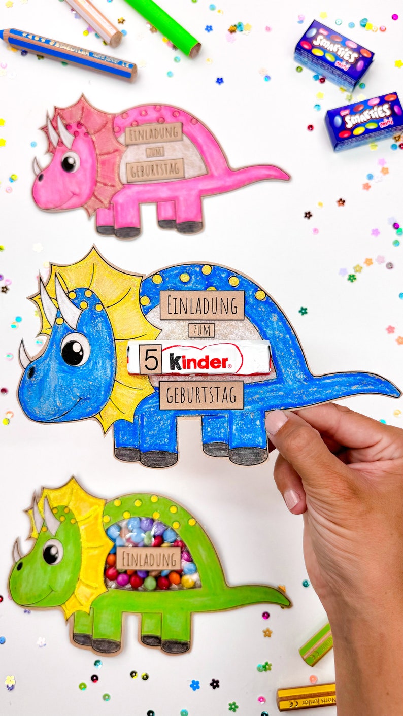 Pu&ograve; includere: Tre inviti di cartone a forma di dinosauro colorati con una finestra ritagliata per leccornie. Il dinosauro rosa dice "Einladung zum Geburtstag", il dinosauro blu dice "Einladung zum 5 Kinder. Geburtstag", e il dinosauro verde dice "Einladung".