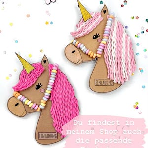 May include: Two pink and white yarn unicorn head cutouts with gold horns and candy bead necklaces. The cutouts have the word "EINLADUNG" printed on them. The text "Du findest in meinem Shop auch die passende Einladung." is printed below the cutouts.