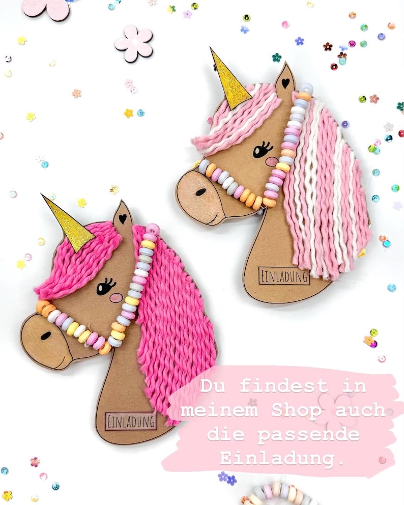 May include: Two pink and white yarn unicorn head cutouts with gold horns and candy bead necklaces. The cutouts have the word "EINLADUNG" printed on them. The text "Du findest in meinem Shop auch die passende Einladung." is printed below the cutouts.