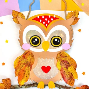 May include: A brown paper owl with large eyes, a red heart, and yellow feet. The owl is decorated with fall leaves and is hanging from a string.
