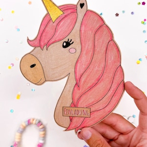 Puede incluir: Un recorte de unicornio rosa y marr&oacute;n con un cuerno dorado y la palabra "Einladung" en una etiqueta marr&oacute;n. El unicornio est&aacute; rodeado de confeti de colores.