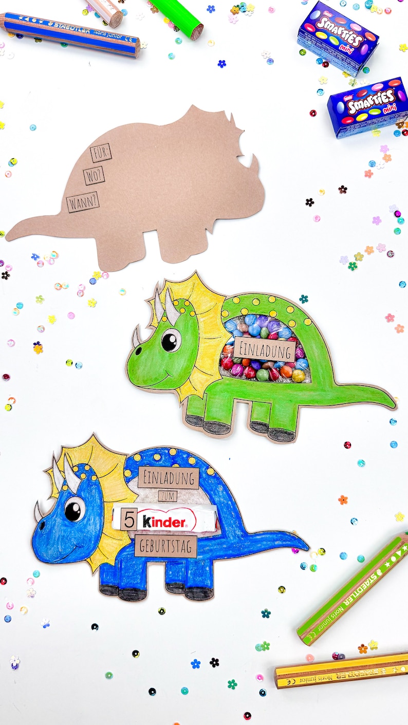 Pu&ograve; includere: Tre scatole per feste a forma di dinosauro, una marrone, una verde e una blu. Le scatole sono decorate con dettagli colorati e hanno una finestra ritagliata per contenere leccornie. La scatola verde &egrave; piena di caramelle colorate, la scatola blu ha una barretta di cioccolato Kinder e la scatola marrone ha un testo che dice "Fur", "Wo?" e "Wann?"
