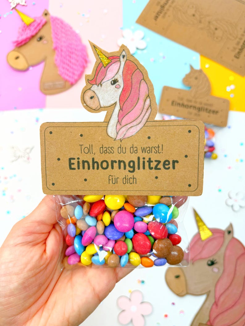 May include: A brown card with a unicorn illustration and the text "Toll, dass du da warst! Einhorn Glitzer f&uuml;r dich."  A clear plastic bag filled with colorful candy is attached to the card.