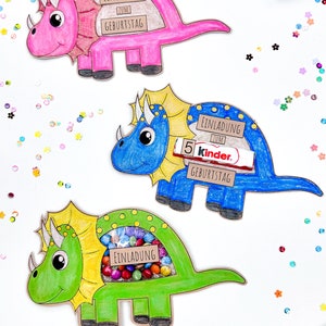 Pu&ograve; includere: Tre artigianati di carta a forma di dinosauro colorati con il testo "Einladung zum Geburtstag" (Invito di compleanno) su ciascuno. I dinosauri sono rosa, blu e verdi. Il dinosauro rosa ha una barretta di cioccolato Smarties all'interno, il dinosauro blu ha una barretta di cioccolato Kinder all'interno e il dinosauro verde ha una variet&agrave; di caramelle colorate all'interno.