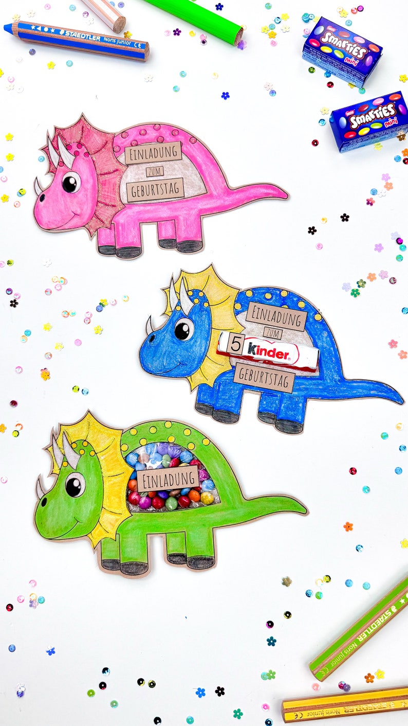 Pu&ograve; includere: Tre artigianati di carta a forma di dinosauro colorati con il testo "Einladung zum Geburtstag" (Invito di compleanno) su ciascuno. I dinosauri sono rosa, blu e verdi. Il dinosauro rosa ha una barretta di cioccolato Smarties all'interno, il dinosauro blu ha una barretta di cioccolato Kinder all'interno e il dinosauro verde ha una variet&agrave; di caramelle colorate all'interno.