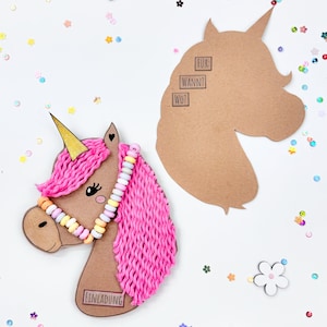 Puede incluir: Una manualidad de unicornio rosa con un cuerno dorado, un collar de caramelos y una crin de hilo rosa. El unicornio est&aacute; sobre un fondo blanco con confeti de colores. El texto "EINLADUNG" est&aacute; en el cuerpo del unicornio. Un recorte separado de cabeza de unicornio de papel marr&oacute;n est&aacute; en el lado derecho de la imagen con el texto "F&Uuml;R: WANN? WO?" en &eacute;l.