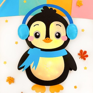 Könnte beinhalten: Ein schwarz-weißer Pinguin mit blauen Ohrenschützern und einem blauen Schal. Der Pinguin befindet sich auf einem weißen Hintergrund mit gelben Sternen und orangefarbenen Blättern.
