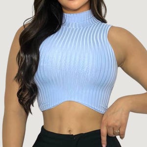 Op de afbeelding: Lichtblauw geribd crop top met een hoge halslijn. De mouwloze top heeft verticale ribbels en een gebogen zoom. Het model draagt een zwarte broek. Een modieuze top voor diverse outfits.
