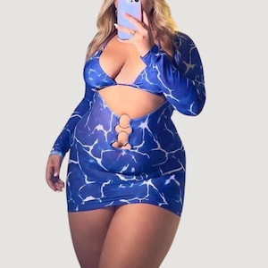 Puede incluir: Un minivestido azul con un estampado de mármol blanco. El vestido presenta mangas largas, un top halter y un diseño recortado con anillos dorados. El conjunto es de dos piezas, incluyendo un top de bikini a juego.