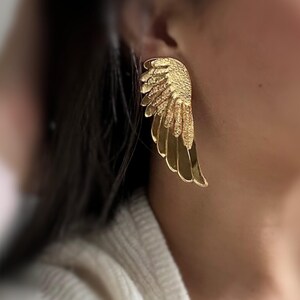 Glossy angel wing earrings with a smooth metallic surface and light comfortable feel. Fine feather details add texture, while the golden shine reflects light softly for a delicate and elegant appearance.