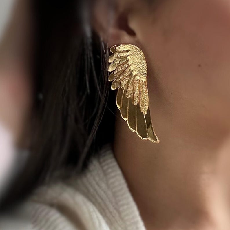 Glossy angel wing earrings with a smooth metallic surface and light comfortable feel. Fine feather details add texture, while the golden shine reflects light softly for a delicate and elegant appearance.