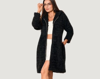 May include: A long-sleeved black fuzzy zip-up jacket with a textured, shaggy exterior. The jacket features a full-length silver-toned zipper down the center, a hood, and two side pockets. It is worn over a plain white top and white shorts.