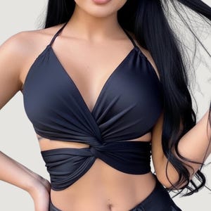 May include: A black halter top with a twisted front design. The top features a deep V-neck and a wrap-around style, showcasing a modern and stylish aesthetic. The fabric appears smooth and form-fitting, suitable for various occasions.