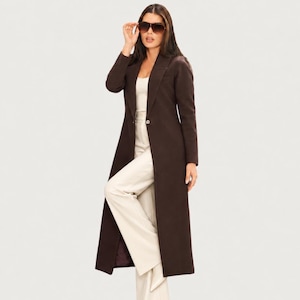May include: A long, dark brown coat with a single-button closure, notched lapels, and long sleeves. The coat is worn over a cream-colored sleeveless top and matching wide-leg trousers. Dark-tinted aviator sunglasses are worn on the face.