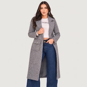 May include: A long, grey, textured wool-blend coat with notched lapels, long sleeves, and two front patch pockets featuring silver-toned button accents. The coat is worn over a white short-sleeved t-shirt with black text and dark blue denim jeans.