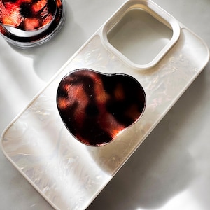 May include: A white phone case with a tortoiseshell pattern phone grip. The case has a raised camera bump and a white background.