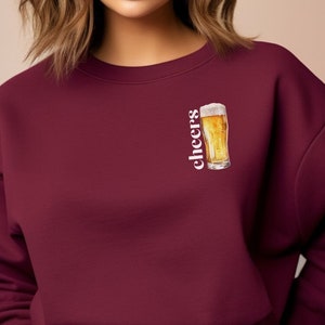 May include: Burgundy sweatshirt with the word "cheers" and a graphic of a glass of beer.
