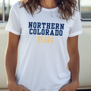 Puede incluir: Camiseta blanca con un gr&aacute;fico azul marino y dorado que dice "NORTHERN COLORADO BEARS"