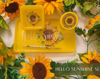 May include: Yellow rolling tray set with a sunflower design and the text "Hello Sunshine". The set includes a small tray, a larger tray, and a small round dish.