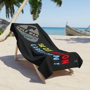Può includere: Asciugamano da spiaggia nero con il testo "GULF WAR" in uno scudo grigio e bianco con un aereo blu e bianco al suo interno. Il testo "1st CAV DIV. 1 ON CARRY ON!" è scritto in giallo, rosso e blu sotto lo scudo. Le lettere "AR" sono nell'angolo in basso a destra.