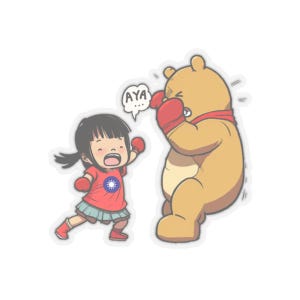 Può includere: Un'illustrazione di cartone animato di una ragazza che indossa guantoni da boxe e una maglietta rossa con la bandiera di Taiwan, che colpisce un orso di cartone animato in faccia. L'orso indossa guantoni da boxe rossi e una sciarpa rossa. La ragazza dice "AYA..." in un fumetto.