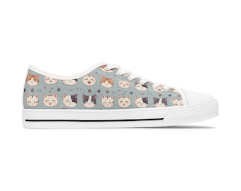 Op de afbeelding: Witte canvas lage sneakers met een blauw en wit patroon van cartoon katten met verschillende gezichtsuitdrukkingen.