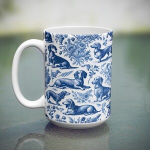 May include: A white ceramic coffee mug featuring a blue and white pattern of dachshunds. The dachshunds are depicted in various poses, including sitting, standing, and running. The mug has a large handle.