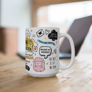 以下が含まれることがあります： 白いセラミック製のマグカップで、ティーカップ、羊、蜂、そして「あなたは十分です」や「自分自身を信じて」などのインスピレーションを与える引用が描かれたカラフルなデザインが施されています。