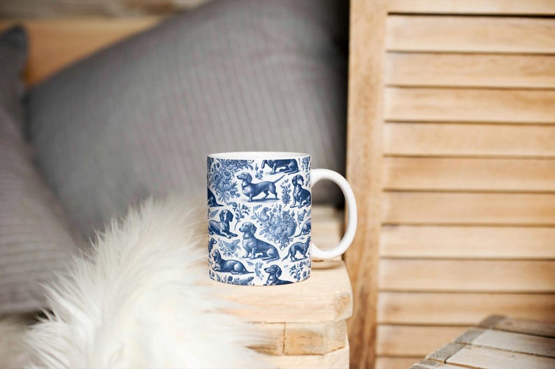 May include: A white ceramic mug with a blue and white pattern of dachshunds. The mug has a handle and is sitting on a wooden surface.