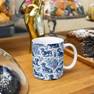 May include: A white ceramic mug featuring a blue and white pattern of dachshunds. The mug is on a wooden table with other items in the background.