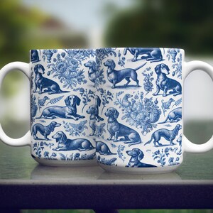 May include: Two white ceramic mugs featuring blue and white illustrations of dachshunds and floral designs.