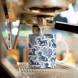 May include: A white ceramic mug with a blue and white pattern of dachshunds. The mug is sitting on a metal rack under a coffee machine.