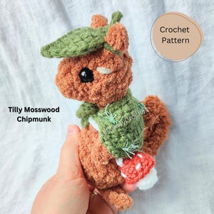 May include: Crochet pattern for a brown and green chipmunk with a mushroom. The chipmunk is wearing a green hat and scarf. The pattern is called "Tilly Mosswood Chipmunk".