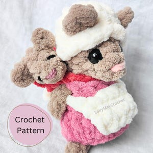 May include: A crochet pattern for a plush toy of a brown and white mouse carrying a smaller brown and white mouse. The larger mouse is wearing a white hat and a pink and white sweater. The smaller mouse is wearing a red scarf. The pattern is available for purchase on Etsy.