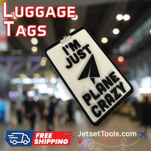 May include: White luggage tag with black border and the text "I'M JUST PLANE CRAZY" with a paper airplane graphic. The words "LUGGAGE TAGS" are in red and white at the top. The tag has a clear plastic loop for attachment.