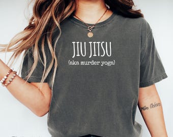 Puede incluir: Una camiseta gris con el texto "Jiu Jitsu (aka murder yoga)" impreso en blanco.