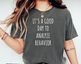 May include: A gray t-shirt with the text "It's a good day to analyze behavior" printed in white. The shirt is being worn by a person with long brown hair.