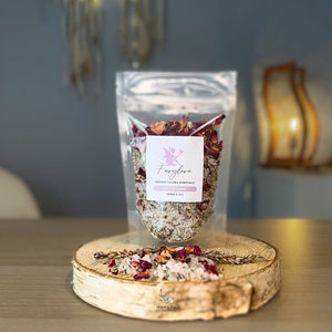 Könnte beinhalten: Ein klarer Plastikbeutel gefüllt mit Badesalzen und getrockneten Rosenblüten, beschriftet mit "Fairylove". Der Beutel steht auf einer Holzscheibe, mit verstreuten Blütenblättern und Kräutern. Das Produkt ist für Bad und Tee.