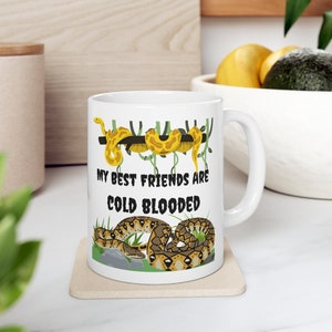 May include: White ceramic mug with a graphic of snakes on a branch and the text "My best friends are cold blooded".