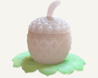 May include: A white ceramic acorn-shaped jar with a lid and a green leaf-shaped base.