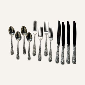 May include: A set of silverware with ornate handles, including spoons, forks, and knives. The silverware is made of polished metal and has a vintage aesthetic.