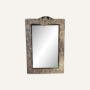 May include: A silver-toned ornate mirror with a black frame. The frame is decorated with intricate floral designs.