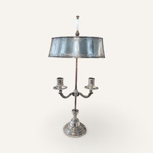 May include: A silver candlestick lamp with a round, ornate shade. The lamp has two candle holders and a decorative base.