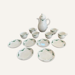 May include: A white porcelain tea set with green floral accents. The set includes a teapot, six cups, and six saucers.