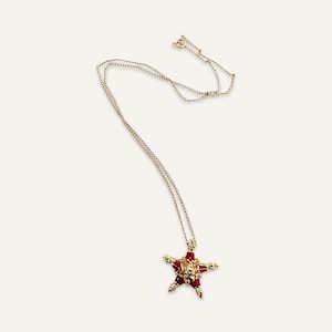 May include: A gold chain necklace with a red star-shaped pendant. The star is made of small red and gold stones.